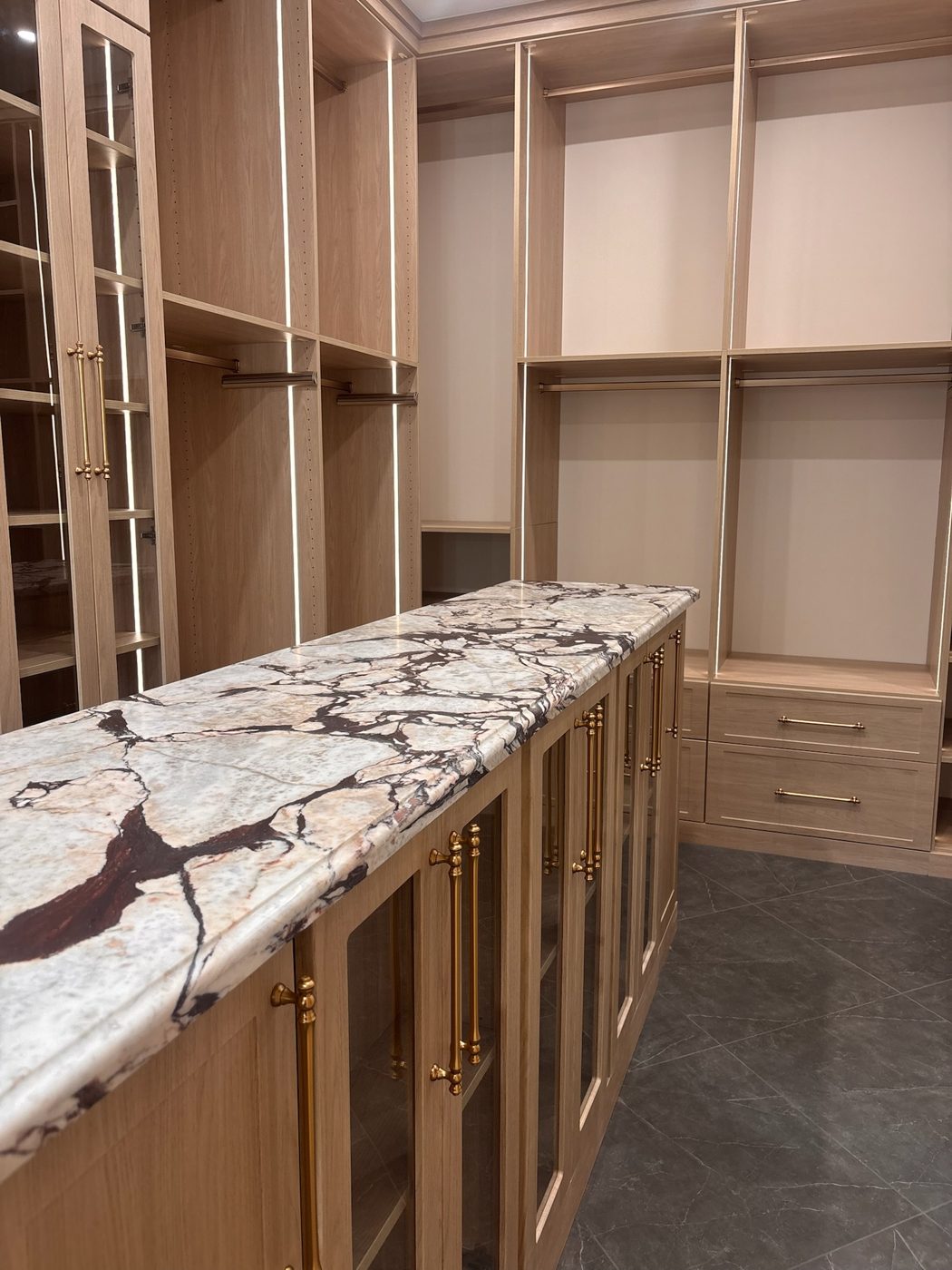 Floor-to-ceiling oak closet wall with glass-front cabinets